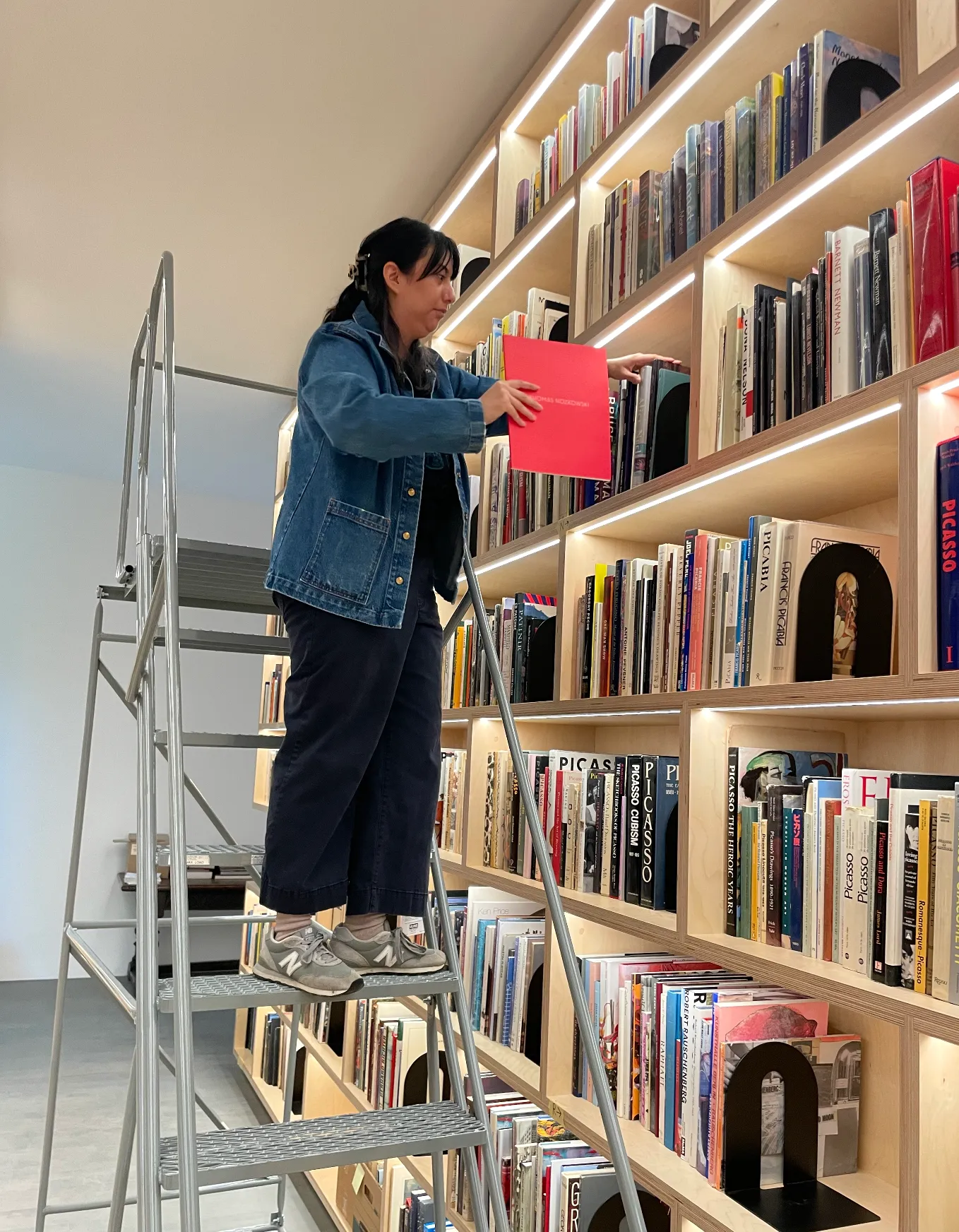 Jennifer arranging white and colored books on high white shelving units