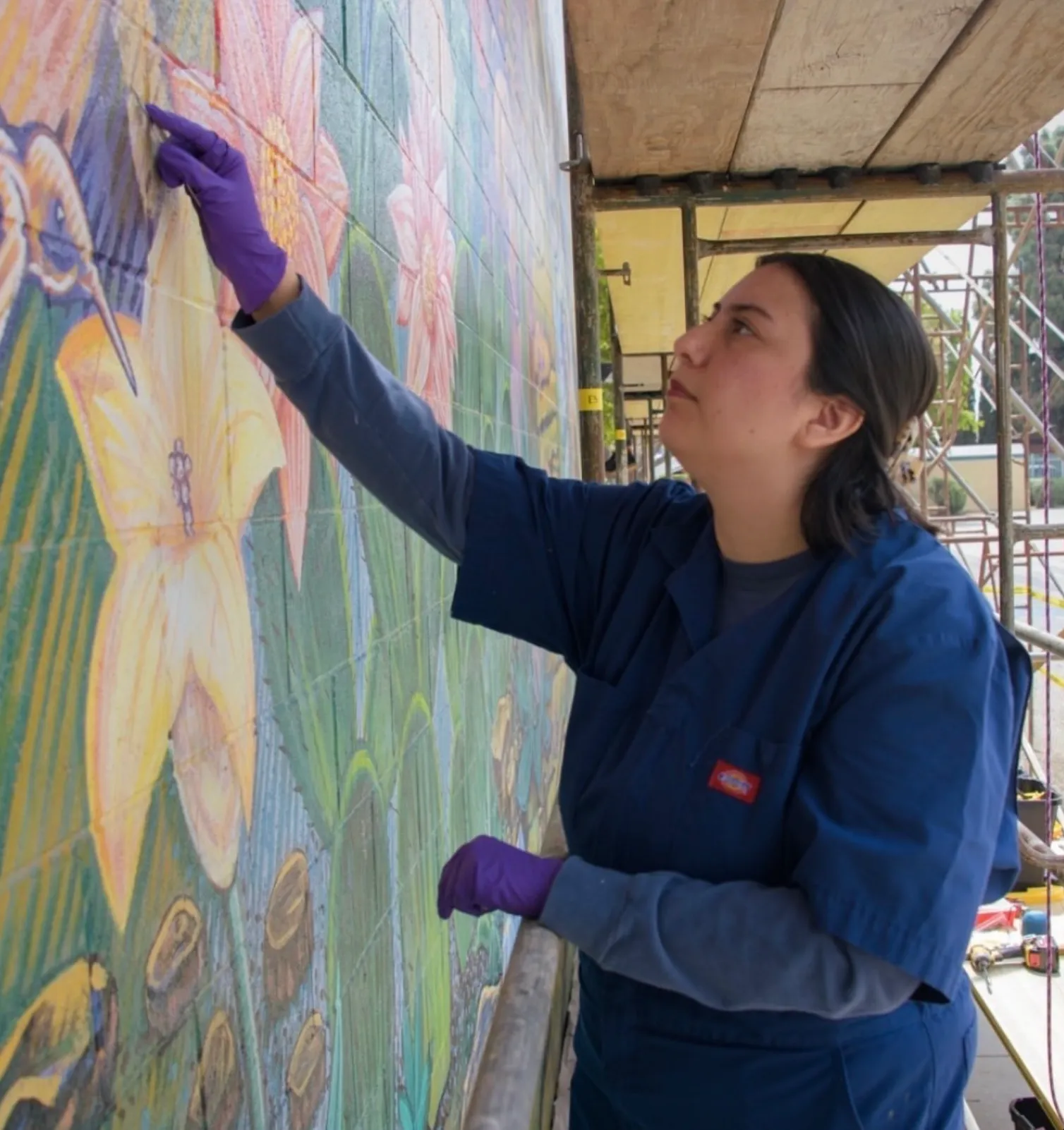 Jennifer working on scaffolding in front of a colorful public mural